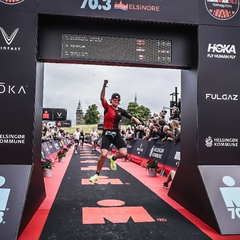 Emilie leaping under the Ironman 70.3 Elsinore finish arch