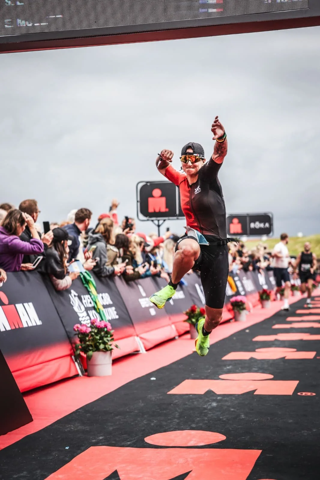 Emilie crossing an Ironman finish line, arms raised, crowd on both sides